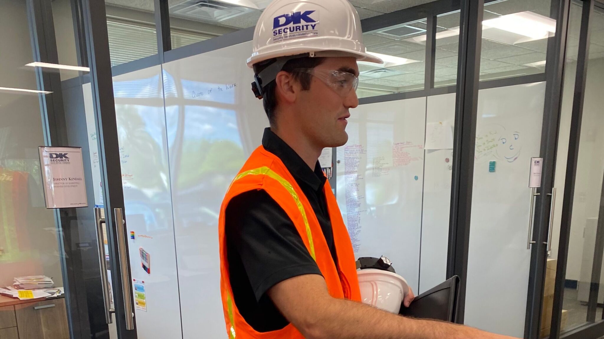 Johnny Kendall stands in the workroom of DK Security's Grand Rapids headquarters adorned with a company safety helmet, goggles, and reflective vest, prior to visiting a client site.