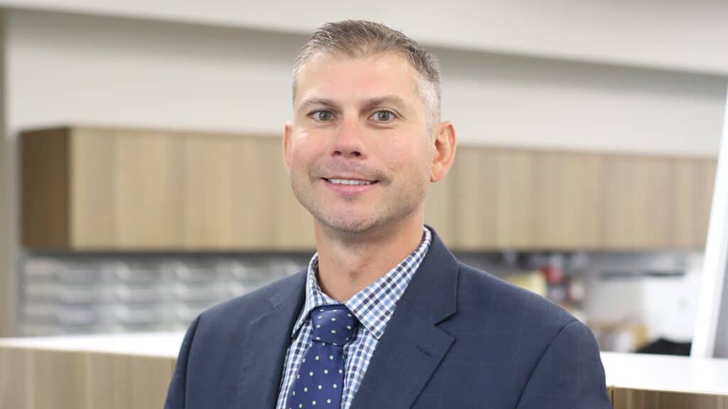 Chief Operating Officer Joe Budnik, dressed in a blue sport coat, stands in DK Security work room for a corporate head shot photo.