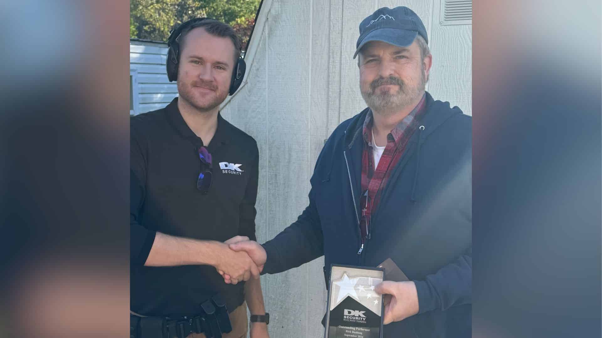 Security officer Rick Bushong shakes hands with DK Security Director of Operations Daniel Verline. In his other hand, Bushong holds an Outstanding Performer award he recently received for exceptional job performance.