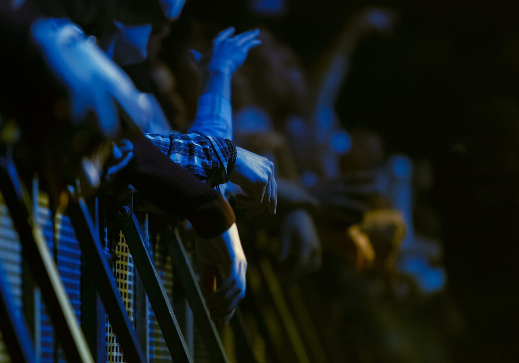 Front row of concert fans behind security fence waiting for the show to start