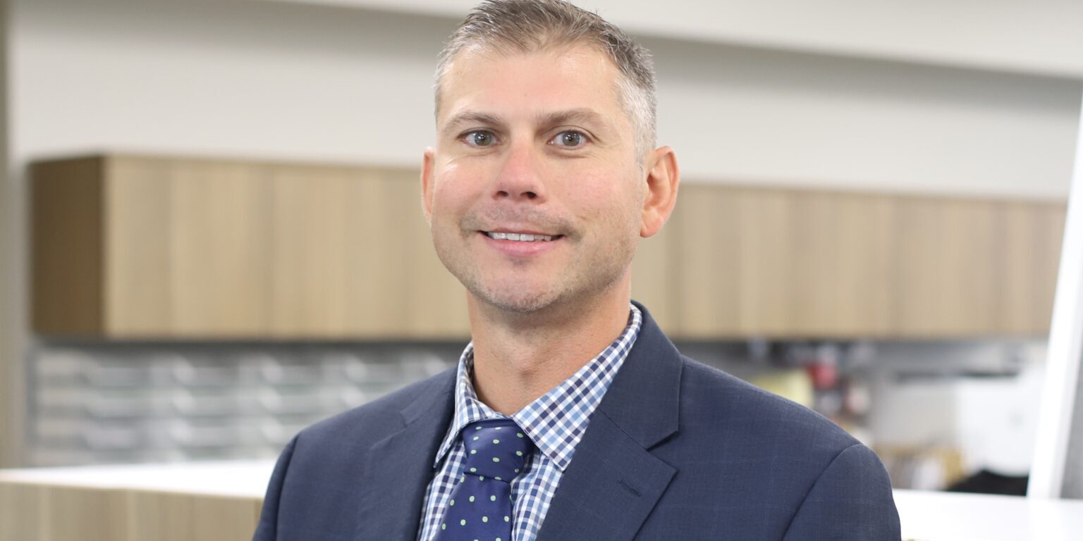 Chief Operating Officer Joe Budnik, dressed in a blue sport coat, stands in DK Security work room for a corporate head shot photo.